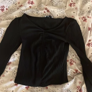 Svart ribbad topp - Säljer en stilren svart ribbad topp med långa ärmar. Perfekt för höst och vinter, den har en elegant v-ringad design som passar både till vardags och fest. Toppen är i bra skick och ger en snygg och figurnära passform. Lite nopprig 