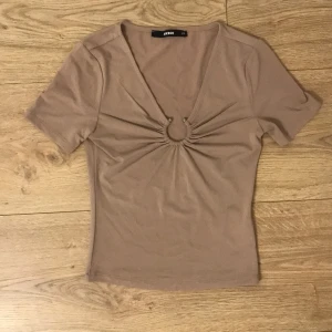 BIKBOK TRÖJA - En oanvänd tröja från bikbok i storlek xs. Den är beige, v-ringad med en metallring i silver. Kortärmad. Pris kan diskuteras.