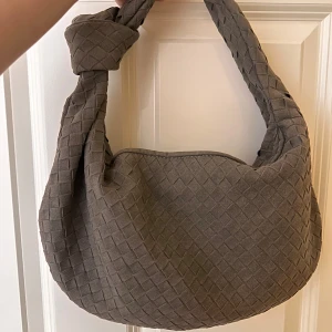 Grå quiltad axelväska - Säljer en snygg grå axelväska med quiltat mönster. Väskan har en praktisk dragkedja och en knutdetalj på axelremmen. Perfekt för både vardag och fest!