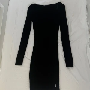 Kort Svart klänning med slit  - Det är en svart, tightare klänning med långa ärmar. Den har en rak, enkel design med en något hög halsringning. Materialet ser ut att vara ett mjukt, stretchigt tyg