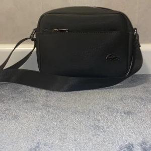Lacost axelväska - Hej! Säljer min axelväska som jag aldrig har använt den är helt fräch och köpt utomlands