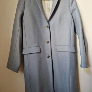 Samsøe & Samsøe ljusblå kavaj, storlek XS - En ljusblå kavaj från Samsøe & Samsøe med knappar framtill och fickor. Kavajen har en rak passform och är tillverkad i ett mjukt material.  Material: Polyester 44% Viscose 28% Wool 26%  Hämtas vid Östermalm