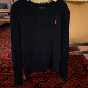 Svart stickad tröja från Polo Ralph Lauren - Säljer en snygg svart stickad tröja från Polo Ralph Lauren. Den har ett klassiskt flätmönster och den ikoniska röda loggan på bröstet. Perfekt för kyliga dagar och ger en stilren look. Passar både till vardags och lite finare tillfällen. Obs den är en barntröja 8-10 år. 