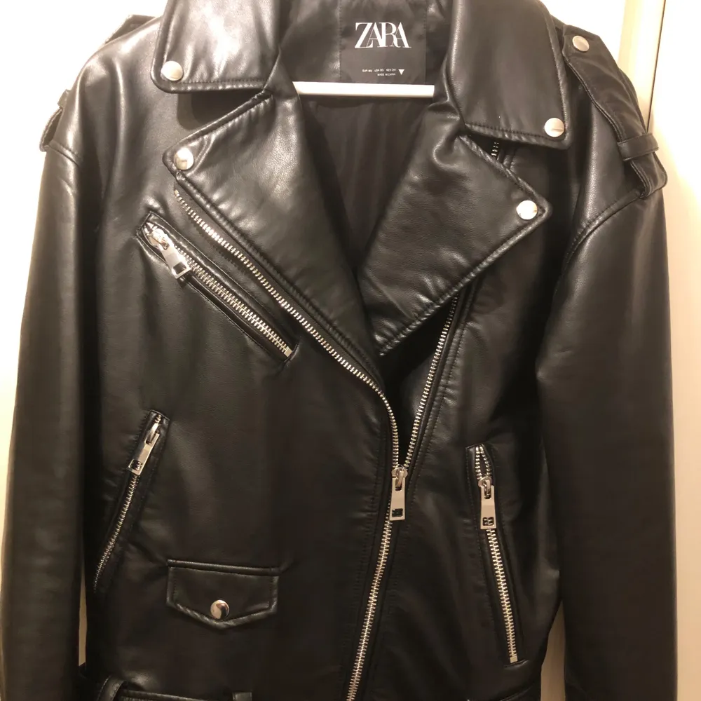 Snygg svart skinnjacka från Zara i klassisk bikerstil. Jackan har flera dragkedjor och en cool bälte-detalj i midjan. Perfekt för en edgy look och passar till nästan allt. Den är i mycket bra skick och redo för nya äventyr!. Jackor.