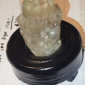 Äkta citrin från Kongo - Säljer en vacker kristall placerad på en rund, mörk träställning. Kristallen har en naturlig, rå form med en ljus, transparent färg som fångar ljuset fint. Perfekt som dekoration eller för samlare av mineraler. Ställningen ger en elegant touch och gör den lätt att placera i hemmet.