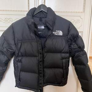 ÄR HELT NYTT!!!  Säljer en svart pufferjacka frän The North Face i storlek M. Jackan är perfekt för kalla dagar med sin tjocka vaddering. Den har en dragkedja framtill och justerbar dragsko i nederkant för extra värme. Superbra skick och redo för vintern!