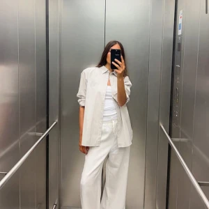 Vita linnebyxor - Säljer ett par vita linnebyxor som är perfekta för sommaren. De har en loose passform och är högmidjade med en bekväm resår i midjan. Byxorna är superlätta och luftiga, vilket gör dem idealiska för varma dagar. Perfekta att styla med en enkel topp eller skjorta för en avslappnad look. ALDRIG ANVÄNDA