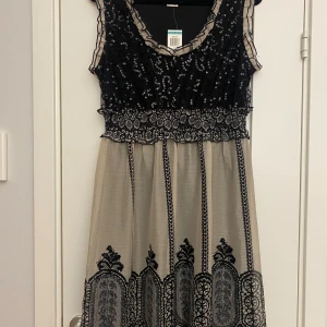 Ny svart och beige klänning i strl XS från American Rag - Ny svart och beige klänning i strl XS från American Rag.  Ny, med prislapp  Mått Över bröstet: ca 52 cm Längd från axeln och ner: ca 98 cm  100% polyester   Kommer från ett djur och rökfritt hem. 