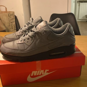 Grå Nike Air Max med reflekterande detaljer - Säljer ett par grå Nike Air Max i mycket bra skick. De har en snygg reflekterande detalj på sidan som verkligen poppar i ljuset. Skorna är i storlek 45 och en halv  har en bekväm passform med klassisk Air Max-dämpning. Perfekta för både vardag och träning!