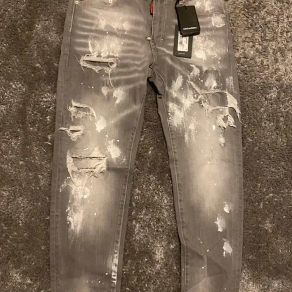 Säljer ett par grå  jeans från Dsq2  i nytt skick. De har en cool distressed look med flera revor och blekta partier. Perfekta för en avslappnad och trendig stil. Passar dem vid längden mellan 180 -190. Jeans & Byxor.