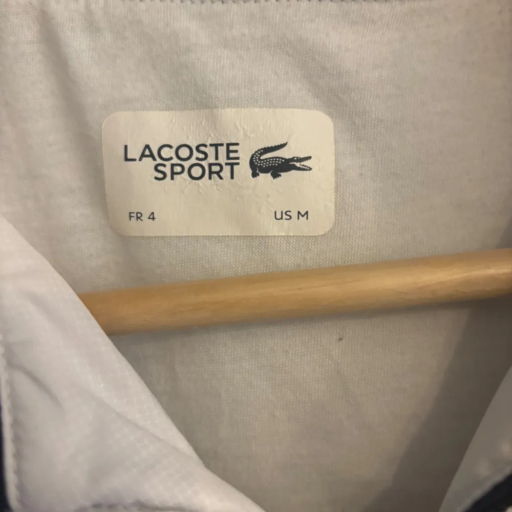 Säljer en snygg vit och marinblå vindjacka från Lacoste Sport. Jackan har gula detaljer och dragkedja framtill. Perfekt för vår och höst med sin lätta och bekväma passform. Den har elastiska muddar och två fickor med dragkedja. Passar både till träning och vardag.. Jackor.