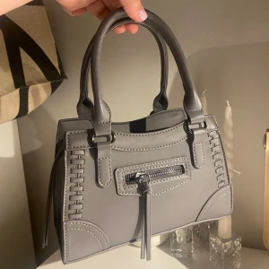 Grå handväska med dragkedja - Snygg grå handväska, Den har en praktisk dragkedja och stiliga sömmar som ger en unik look. Den har även två innerfickor, använd fåtal gånger och inga defekter👜