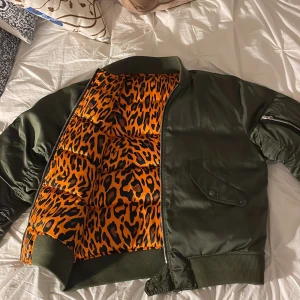 Olivgrön bomberjacka från Sandro - Säljer en snygg olivgrön bomberjacka från Sandro med ett coolt leopardmönstrat foder. Jackan har dragkedja och ribbade muddar vid ärmslut och nederkant. Perfekt för vintern! 🐆