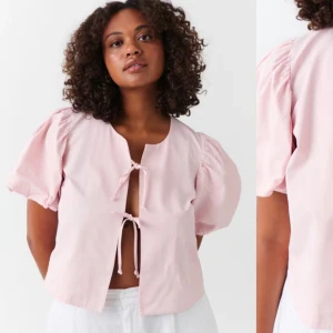Rosa blus med knytning - Säljer en söt rosa blus med korta puffärmar och knytning framtill. Perfekt för vår och sommar! Blusen har en luftig passform och är gjord i ett lätt material som känns skönt mot huden.