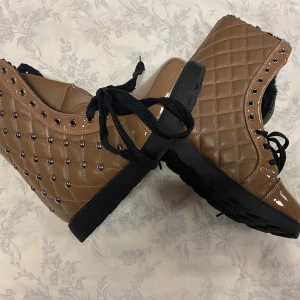Bruna quiltade boots med snörning - Snygga bruna boots i quiltat mönster med glansig finish och svarta snören. De har en mysig, fodrad insida som passar perfekt för kyligare dagar. Dekorerade med små nitar för en extra touch av stil. Perfekta för höst och vinter!  Stlk kvar 36,37,38 ,39 och 40.         Tjocka fleece inuti, rekommenderar att välja 2 Stlk större än som är vanlig i storlek , till exempel storlek 39 passar som är Stlk 37 i vanligt storlek 