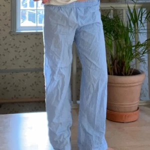 Blå- och vitrandiga byxor från Gina Tricot - Säljer ett par bekväma blå- och vitrandiga pyjamasbyxor från Gina Tricot i storlek S. Perfekta för en avslappnad dag hemma eller sommarens lata dagar. Byxorna har en loose passform och är gjorda i ett mjukt bomullsmaterial. De har en elastisk midja för extra komfort.