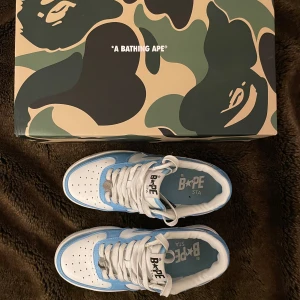 Blå och vita sneakers från A Bathing Ape (BAPE) (BAPESTA) - Säljer ett par snygga BAPESTA sneakers i blått och vitt. Skorna är i nytt skick och kommer med extra blåa skosnören och Dust-Bag. Originalförpackning medföljer. Skullr säga att storleken är mer för 39.
