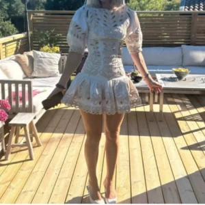 Vit klänning med spetsdetaljer från Maje - Säljer en superfin vit klänning från Maje med vackra spetsdetaljer och puffiga ärmar. Den har en tight passform upptill och en volangkjol som ger en söt look. Perfekt för sommarens fester, midsommarfirandet eller student! Klänningen är i mycket bra skick och har en dragkedja i ryggen för enkel påklädning.