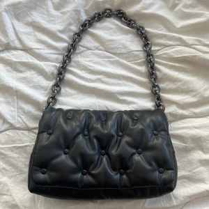 Zara väska  - Säljer en snygg svart axelväska i quiltat skinn med en cool kedja som axelrem. Väskan har en stilren design med knappliknande detaljer och en praktisk dragkedja inuti. Perfekt för både vardag och fest! 🖤