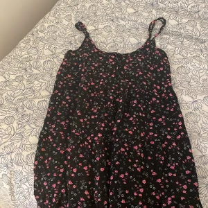 Blommig klänning från FB Sister - Söt blommig klänning från FB Sister i svart med rosa och vita blommor. Klänningen har knappar framtill och smala axelband, perfekt för sommardagar. Den är i mycket bra skick och passar både till vardags och festligare tillfällen.