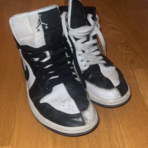 Svartvita Nike Air Jordans - Säljer ett par klassiska svartvita Nike Air Jordans i bra skick. Skorna har en hög modell med snörning och den ikoniska Air Jordan-loggan på sidan. Perfekta för både vardag och fest! De har lite slitage men är fortfarande riktigt snygga och bekväma. Du kan absolut putsa upp de själv! Skolåda medkommer ej!