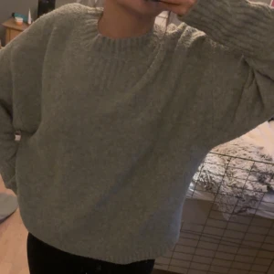 Grå stickad tröja - Mysig grå stickad tröja som är perfekt för kyliga dagar. Den har en avslappnad passform och långa ärmar, vilket gör den superbekväm att ha på sig. Perfekt för både höst och vinter!