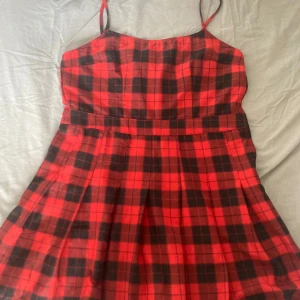 Röd och svart rutig klänning från Divided - Säljer en superfin röd och svart rutig klänning från Divided H&M. Den har smala axelband och en dragkedja i sidan för enkel påklädning. Perfekt för höst och vinter med ett par snygga boots eller sneakers. Klänningen är i storlek 44!