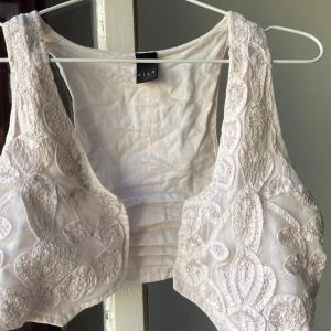 Vit broderad topp från Vila - Säljer en superfin babyrosa väst från Vila med vackra broderade detaljer. Kan användas som topp också! unik design med ett blommigt mönster. Perfekt för layering. Några små gråa fläckar som ej syns vid användning, se sista bild!  S/M