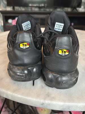 Nike Air Max Plus Tn helsvarta sneakers - Säljer ett par helsvarta Nike Air Max Plus Tn sneakers med den klassiska Tn Air-loggan bak. Skorna har en chunky sula och meshdetaljer på ovandelen. Perfekta för dig som gillar streetwear och vill ha en ikonisk modell i garderoben.