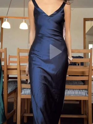 Marinblå balklänning i satin - Snygg marinblå långklänning i glansigt satinliknande material med v-ringning och smala axelband. Klänningen har en figurnära passform och elegant siluett som ger en stilren look. Perfekt för dig som vill ha en klassisk balklänning till studenten! 