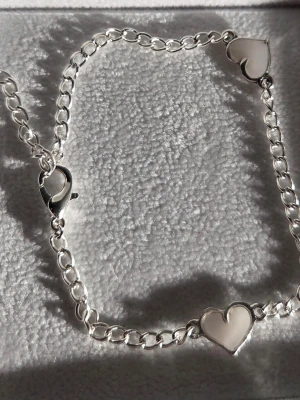 Silverarmband med lysande hjärtan - Snyggt silverfärgat armband med två vita hjärtformade detaljer som lyser lila i mörker. Armbandet har kedjelänkar i rostfritt stål och ett klassiskt lås. Perfekt för dig som vill ha något unikt och coolt på handleden. Längden är ca 20 cm, vill du ha en annan längd så kan du bara skriva till mig så ordnar jag det 💖