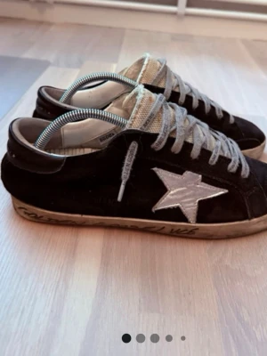 Golden Goose  - Svarta sneakers från Golden Goose med ikonisk vit stjärna på sidan, grå mesh-plös och grå skosnören med logotyp. Ovandelen är i mocka och sulan har handskrivna detaljer. Klassisk low-top modell som ger en cool och avslappnad vibe.