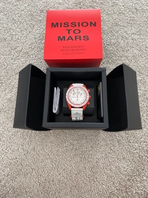 Omega x Swatch Mission to Mars klocka - Säljer en Omega x Swatch Speedmaster MoonSwatch Mission to Mars. Klockan har en vit urtavla med röda detaljer och röd boett. Armbandet är vitt med svart text och logga. Tillverkad i biokeramik och levereras i originalbox.