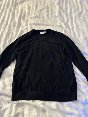 Svart stickad tröja från VILA - Klassisk svart stickad tröja från VILA med rund halsringning och ribbade muddar vid ärmslut och nederkant. Perfekt basplagg som är lätt att matcha till olika outfits. Materialet ser mjukt och bekvämt ut, och tröjan har en enkel, stilren design. Nopprig lite grann