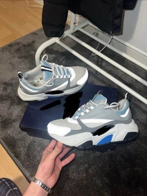  sneakers i grått och blått b22 - Säljer ett par chunky sneakers med cool design i grått, vitt och blått. Skorna har meshdetaljer, reflekterande partier och tjock sula. Perfekta för dig som gillar streetwear och vill sticka ut med dina skor.skriv för mer info 