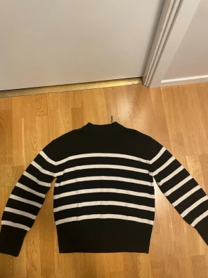 Svartvit randig stickad tröja - Säljer en svart stickad tröja med vita horisontella ränder. Tröjan har lång ärm, ribbstickade muddar och en högre rund halsringning. Perfekt för dig som gillar klassiska mönster och vill ha en skön, stilren look.