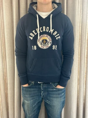 Abercrombie & Fitch hoodie blå - S - Fint skick, inga defekter (slitningarna på hoodien hör till). Står stolek L på lappen men den sitte som en S. Modellen på bilden är ca 180 cm. Om du undrar över något tveka då inte på att höra av dig!