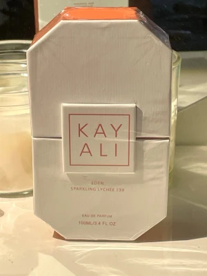 Kayali Eden Sparkling Lychee 100ml - Kayali Eden Sparkling Lychee 39 är en Eau de Parfum i en lyxig, rosa glasflaska med gulddetaljer och en kristallformad kork. Doften har fruktiga och blommiga inslag, och flaskan rymmer 100 ml. Förpackningen är vit med rosa detaljer och modern design.