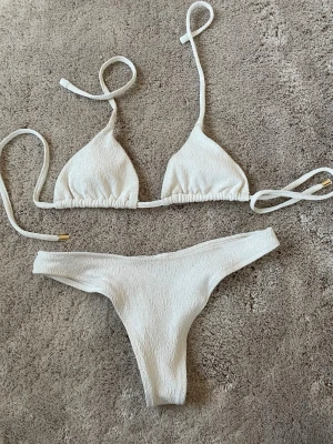 Vit bikini med snörning - Stilren vit bikini med trekants-bh och smala knytband både upptill och i sidorna. Materialet har en lätt struktur som ger en trendig look. Perfekt för lata dagar på stranden eller poolen.