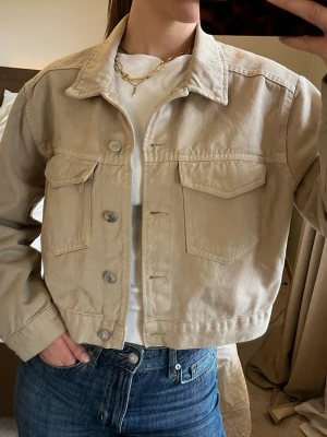 Beige jeansjacka - storlek M - Beige vårjacka i jeansmaterial, 100% bomull - Ginatricot   Silvriga knappar och två bröstfickor Storlek M  Aldrig använd