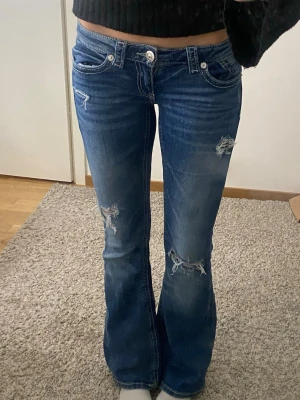 Blå bootcut jeans med hål - Blå lågmidjade bootcut jeans ifrån Gina tricot med hål och med detaljerade fickor.