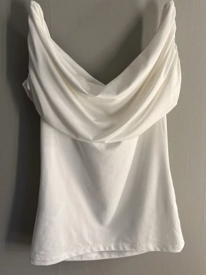 Vit draperad ärmlös topp - Säljer en stilren vit topp med snygg draperad urringning och ärmlös design. Tyget är mjukt och följsamt, perfekt för dig som gillar minimalistisk och trendig stil. Passar till många olika outfits och är lätt att matcha.