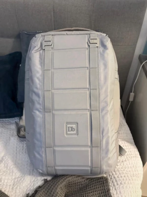 Db The Carryall 40L Ryggsäck - Snygg ljusgrå ryggsäck från Db med stilren, fyrkantig design och tydliga sömmar. Väskan har vadderade axelband, praktiskt bärhandtag och flera fack. Tillverkad i slitstarkt syntetmaterial, perfekt för dig som gillar minimalistisk look. 40 liter utrymme. Använd fåtalls gånger. Skick 9/10: inga defekter, bara lite smutsig som man kan få bort. Vid frågor och funderingar så hör av er🙌
