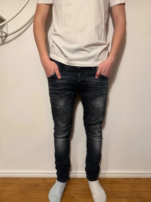 Gråa slimfit jeans med slitningar från jack&jones  - Säljer ett par gråa slimfit jeans med snygga slitningar och tvättade detaljer på låren och knäna. Jeansen har klassisk femficksmodell och smal passform soppar till en modern look. Perfekta till en avslappnad stil. W30 L32