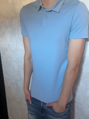 Ljusblå pikétröja med krage - Snygg ljusblå pikétröja med klassisk krage och korta ärmar. Tröjan har två knappar vid halsen och är tillverkad i mjukt bomullsmaterial. Perfekt för en clean och enkel stil.