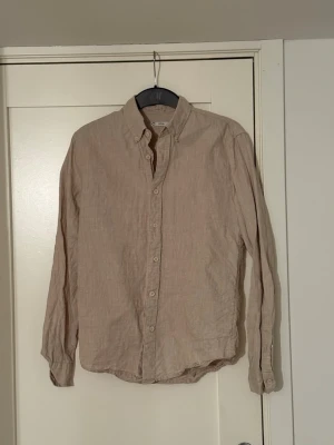 Beige linneskjorta - Säljer en stilren beige skjorta från Cubus i 100% linne. Skjortan har klassisk button-down krage, långa ärmar och vita knappar framtill. Perfekt för en avslappnad men ändå snygg look. Passar till både jeans och chinos. Köpt för typ 500