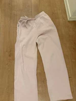 Ljusrosa mjukisbyxor med dragsko - Säljer ett par ljusrosa mjukisbyxor med resår i midjan och dragsko. Byxorna har raka ben och är tillverkade i ett mjukt och bekvämt material, perfekta för chill dagar. Inga synliga loggor eller märken.