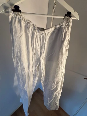 Vita linnebyxor med resårmidja - Säljer ett par vita linnebyxor med avslappnad passform och resår i midjan. Byxorna är tillverkade i ett lätt och luftigt linnetyg, perfekta för varma dagar. Klassisk rak modell utan synliga fickor eller detaljer. Se bilderna för att se fläckarna som finns!