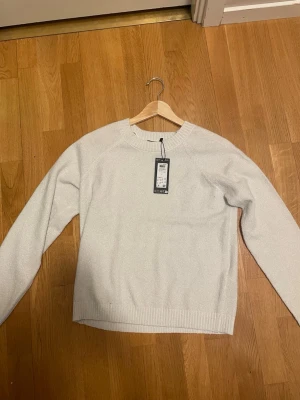 Vit stickad tröja från Vero Moda - Snygg vit stickad tröja från Vero Moda med rund halsringning och ribbade muddar vid ärmslut och nederkant. Tröjan har en enkel och clean design som passar perfekt till jeans eller kjol. Materialet är mjukt och bekvämt.glittertröja 