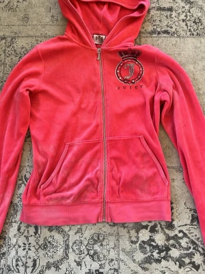 Rosa velour hoodie från Juicy Couture - Säljer en ikonisk rosa velour hoodie från Juicy Couture med dragkedja, fickor fram och huva. Framsidan har ett glittrigt Juicy-märke och baksidan har ännu en juicy logo. Perfekt för dig som gillar Y2K eller Mcbling. Den är XL men passar mer som en M. Den är lite missfärgad längst ner vid både ärmarna och på en ficka. Skriv om du har frågor eller för mer bilder, pris är diskuterbart 💖